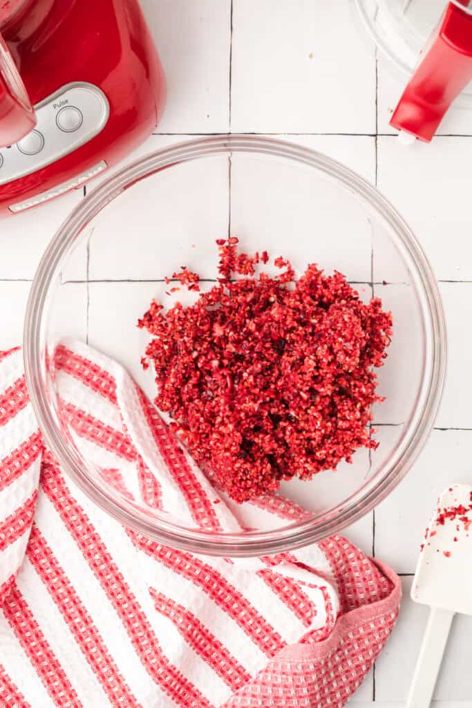 Morceaux d'orange finement hachés à l'intérieur du robot culinaire rouge, montrant un mélange jaune-orange vif.