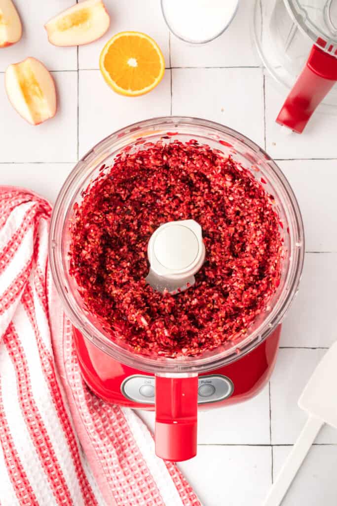 Morceaux d'orange finement hachés à l'intérieur du robot culinaire rouge, montrant un mélange jaune-orange vif.