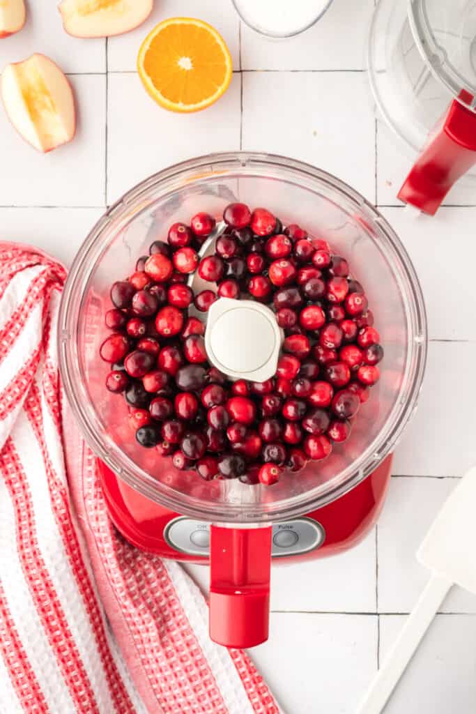 Morceaux d'orange finement hachés à l'intérieur du robot culinaire rouge, montrant un mélange jaune-orange vif.