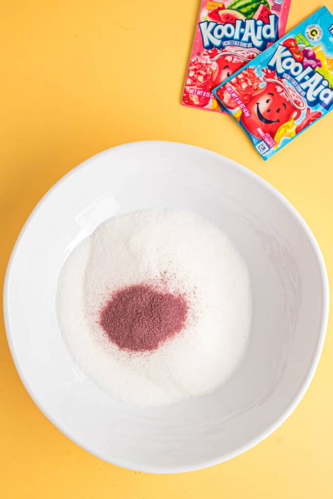 Bol de sucre avec un monticule de poudre Kool-Aid sur le dessus, sachets de Kool-Aid en arrière-plan.