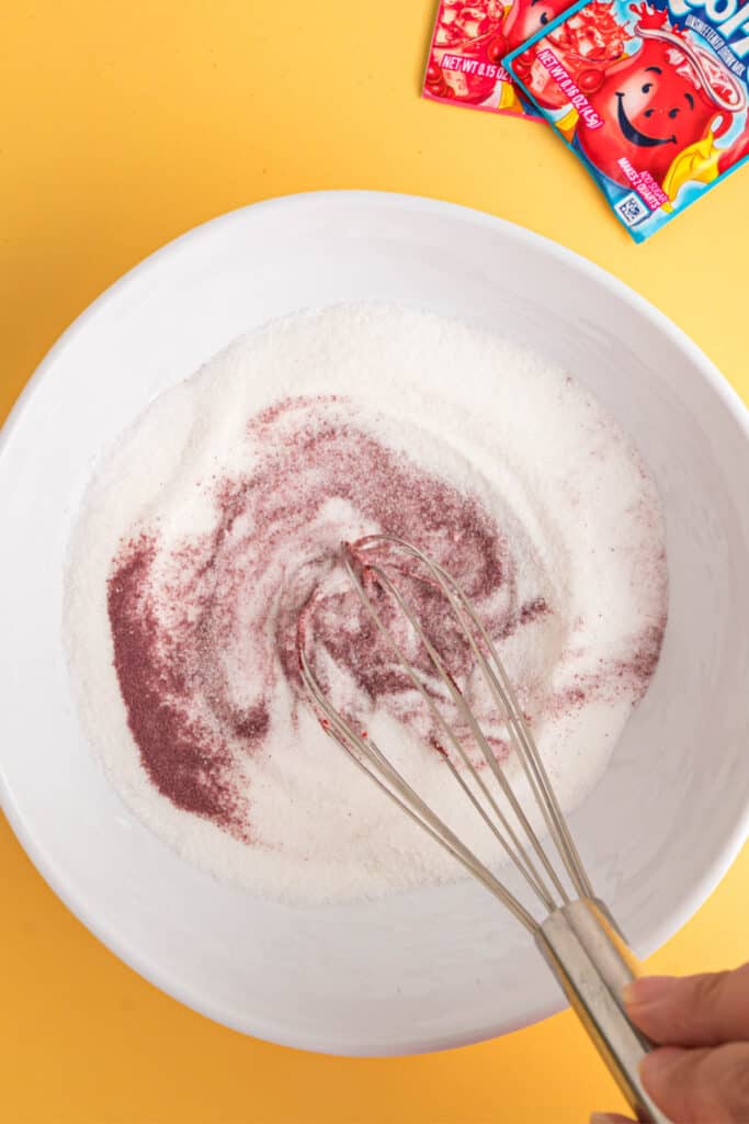 Fouet mélangeant le sucre et la poudre de Kool-Aid dans un bol blanc.