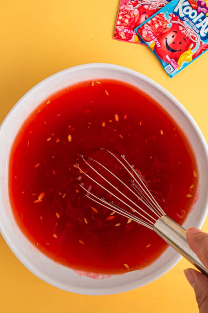 Fouet mélangeant la saumure de cornichons et le mélange Kool-Aid dans un bol blanc.