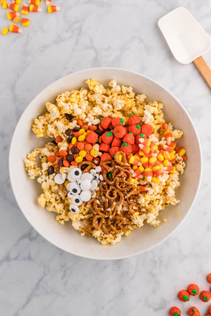 Pop-corn dans un bol à mélanger garni de bretzels, de maïs soufflé, de citrouilles en bonbon, de morceaux de Reese et de globes oculaires en bonbon avant de remuer.